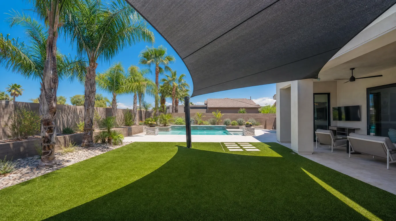 Arizona backyard with green artificial turf shaded by a modern shade sail beside a pool in bright summer sun