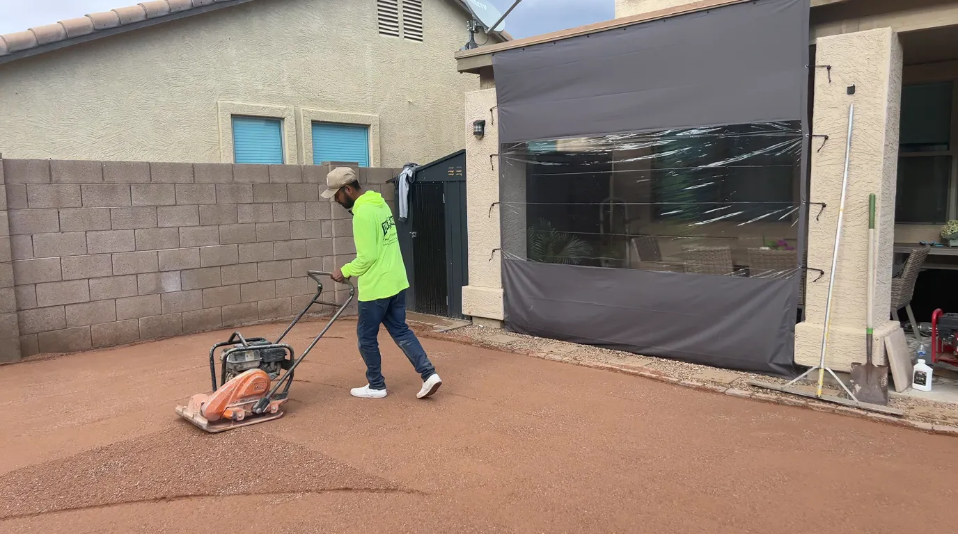 A Turf Yard crew member running a plate compactor over the base before laying artificial turf in an Arizona backyard