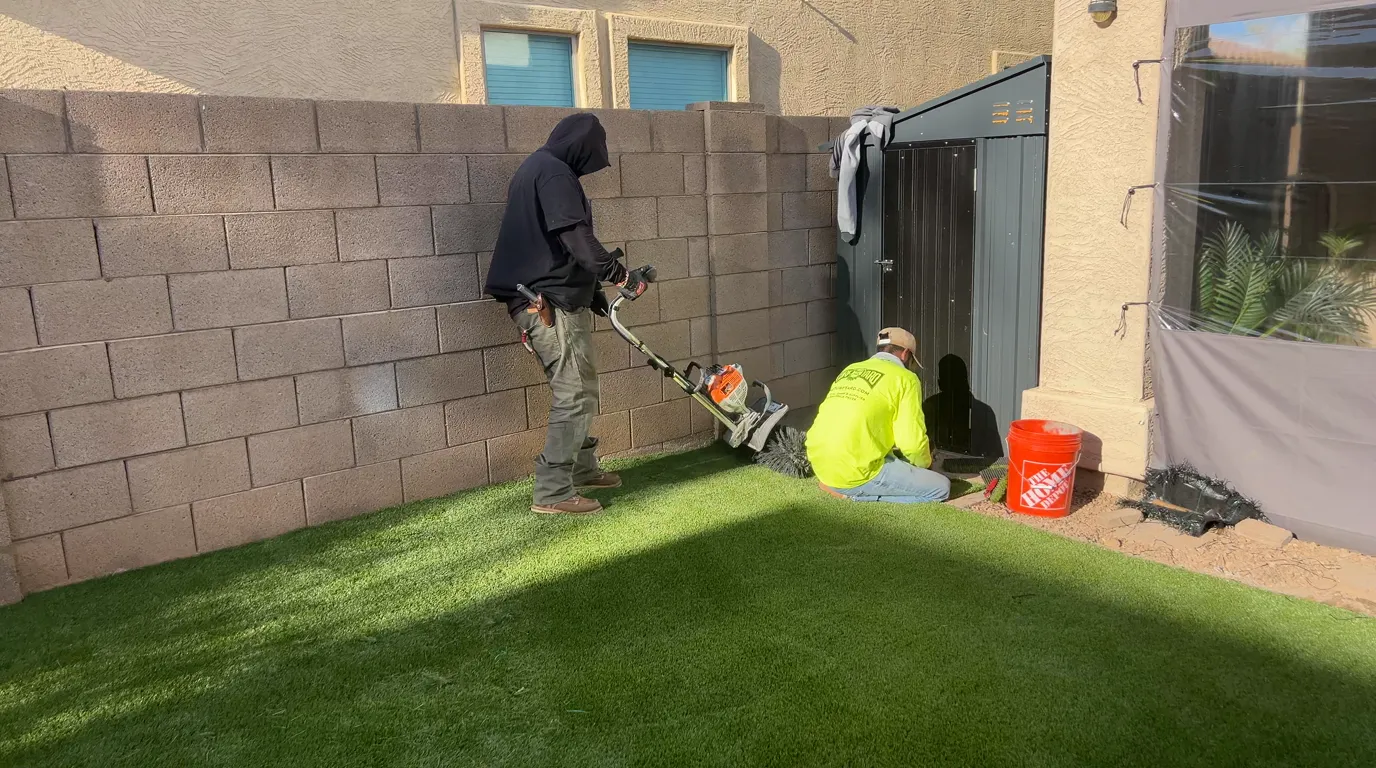 A crew member securing artificial turf along the block-wall edge of a backyard