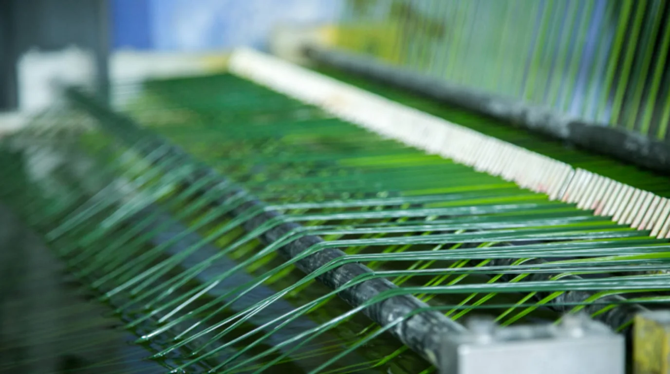Strands of green polyethylene turf yarn running through an artificial grass manufacturing machine