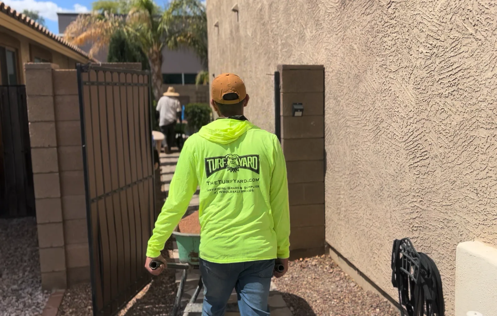 A Turf Yard crew member walking a wheelbarrow of base material into a backyard ahead of an artificial turf installation
